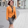Dame im Business-Look mit sommerlichen Loop-Schal passend zum organgen Blazer und dem braun-grauen Rock in der Fußgängerzone einer Stadt