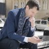 Geschäftsmann mit blauem Herrenschal von il-Design auf einer Bank sitzend ins Handy blickend