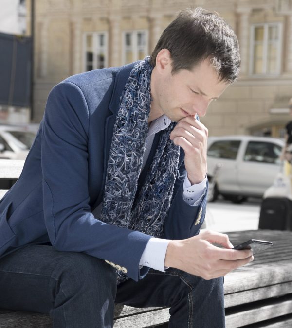 Geschäftsmann mit blauem Herrenschal von il-Design auf einer Bank sitzend ins Handy blickend