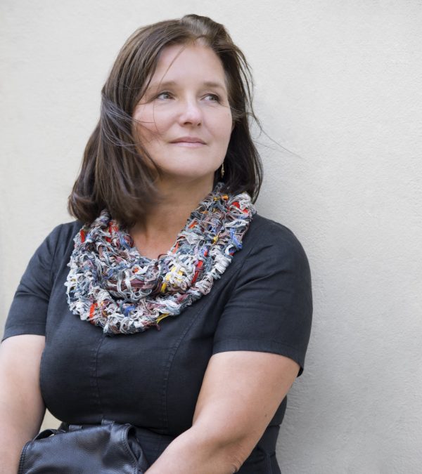 Frau mit sommerlichen Loopschal passend zum schwarzen Abendkleid vor einer Hausmauer wartend