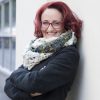 lächelnde Frau in der kalten Jahreszeit vor einer Hausmauer bekleidet mit grauem Lodenmantel und elegantem Winter-Loop in Petrol, Grün und Orangel Damen, Kunst und Mode, Damenmode, handgemacht, handgefertigt, Wolle, il-design